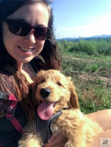 woman with golden doodle puppy on lap smiling on mountaintop